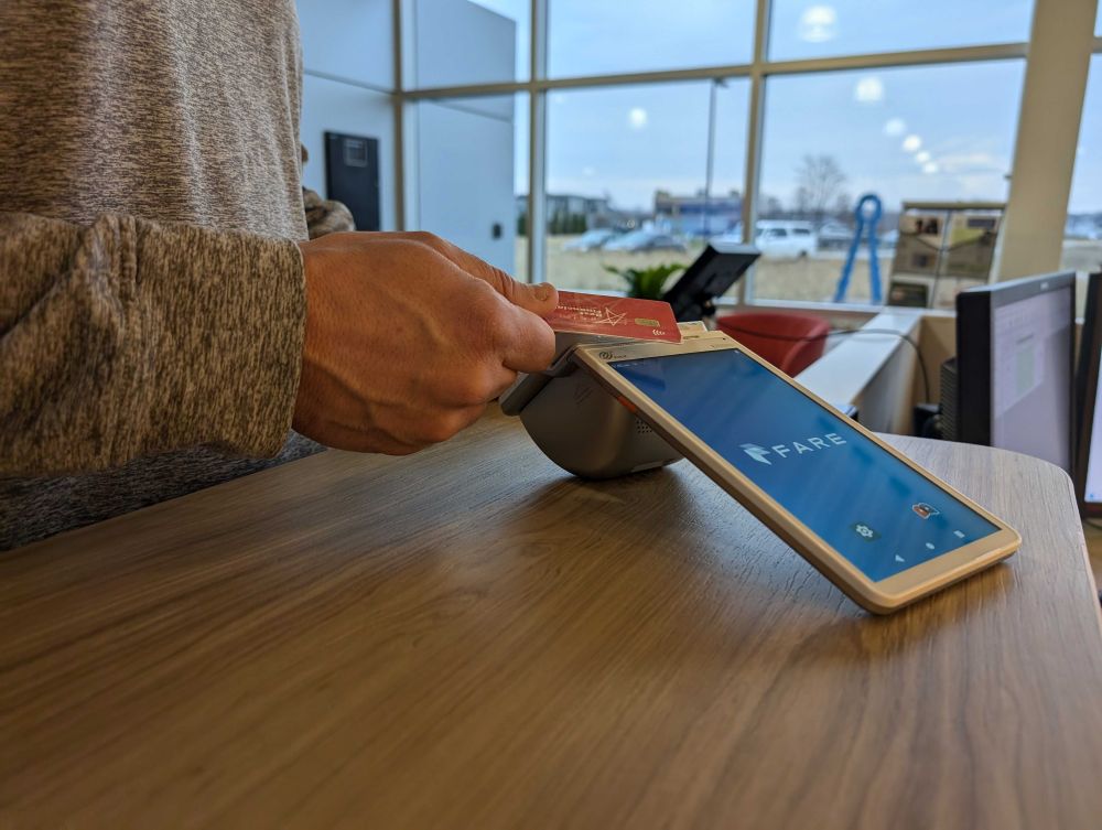 A customer holds a credit card to the Fare terminal sitting on the counter