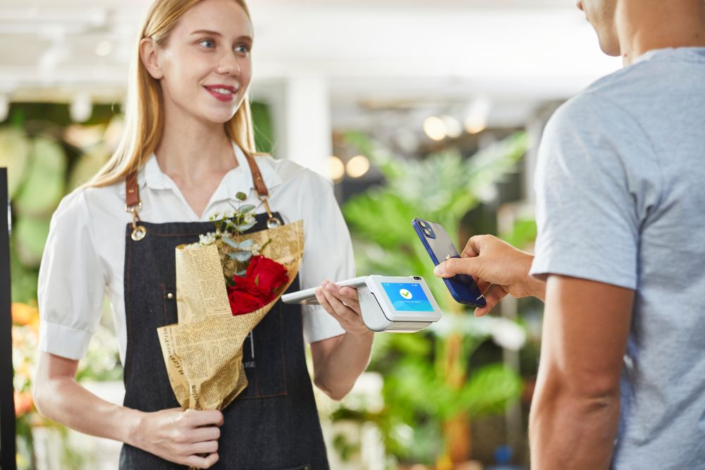 A female flower shop owner holds a Fare terminal while a male customer pays with his smartphone